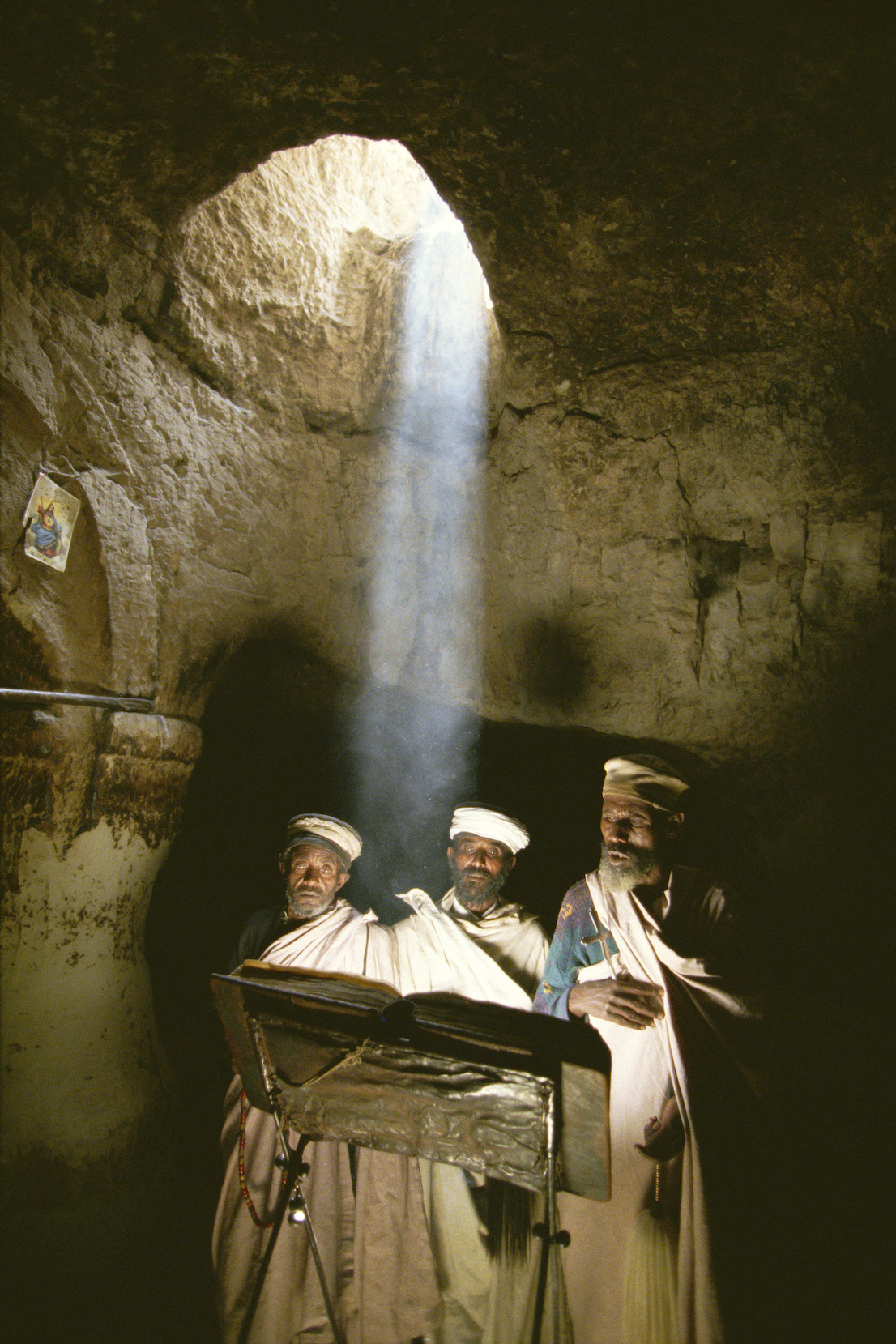 Foto di Kazuyoshi Nomachi. Un gruppo di sacerdoti prega nella chiesa di Abuna Aron poco dopo mezzogiorno, quando da un oculo della volta i raggi del sole scendono a perpendicolo nella chiesa scavata nella roccia. Nei pressi di Lalibela, Etiopia, 1996.