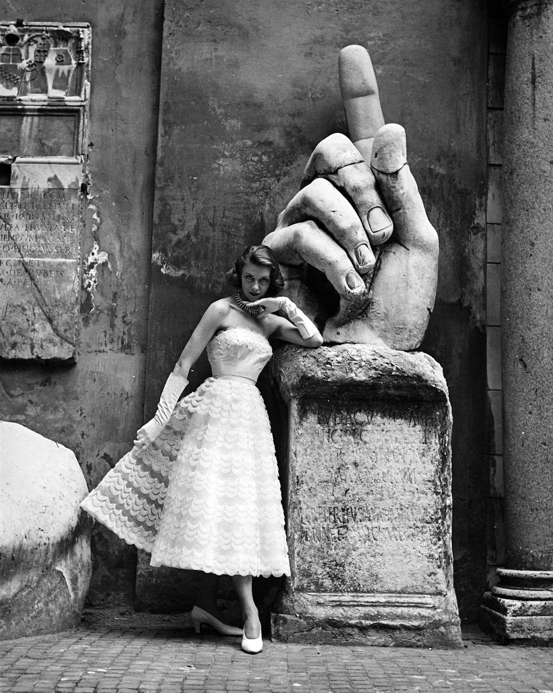La modella, fotografata ai Musei Capitolini davanti alla mano della statua monumentale di Costantino I, indossa un modello delle Sorelle Fontana (pubblicata sulla rivista La Donna) Foto di Regina Relang, 1952. Courtesy Münchner Stadtmuseum, Sammlung Fotografie, Archiv Relang.